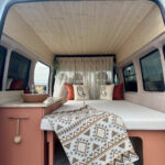 Off-grid van interior with wooden ceiling and cozy bedding setup.
