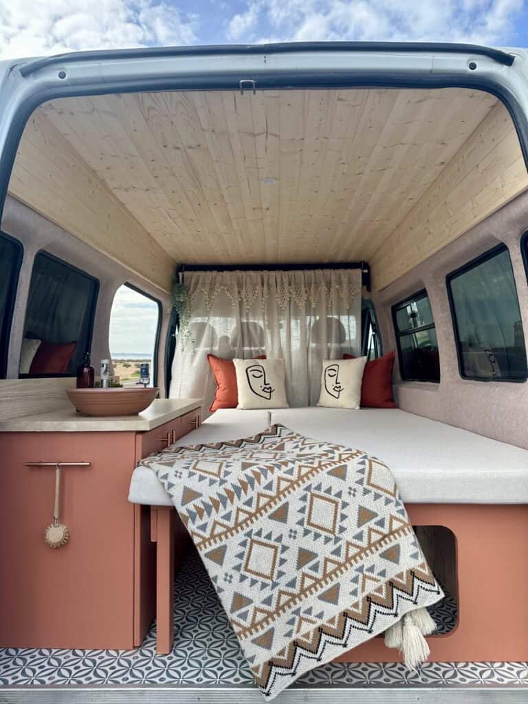 Off-grid van interior with wooden ceiling and cozy bedding setup.