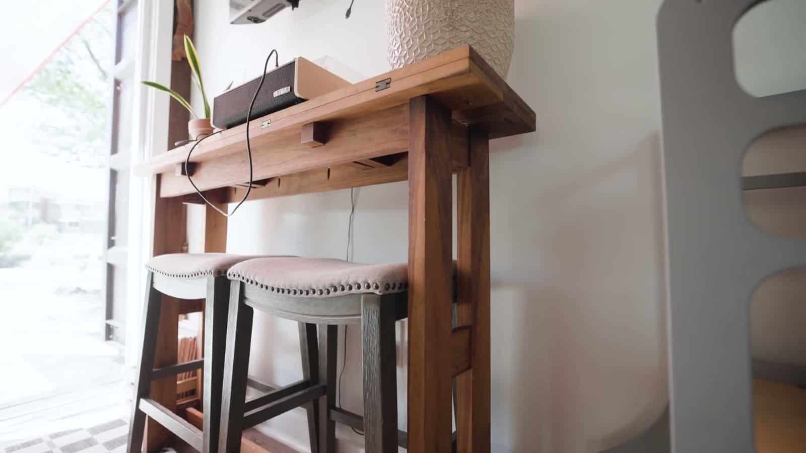 Narrow wood console desk with a record player and two upholstered bar stools beside the sliding glass doors of a container home