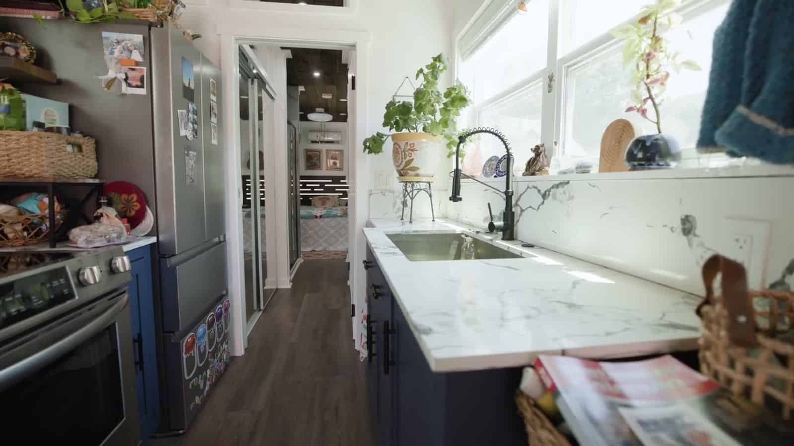 Galley kitchen in a container home with navy cabinets, white marble-look counters, an undermount sink with a black faucet, a stainless range and refrigerator, and a hallway running to the back