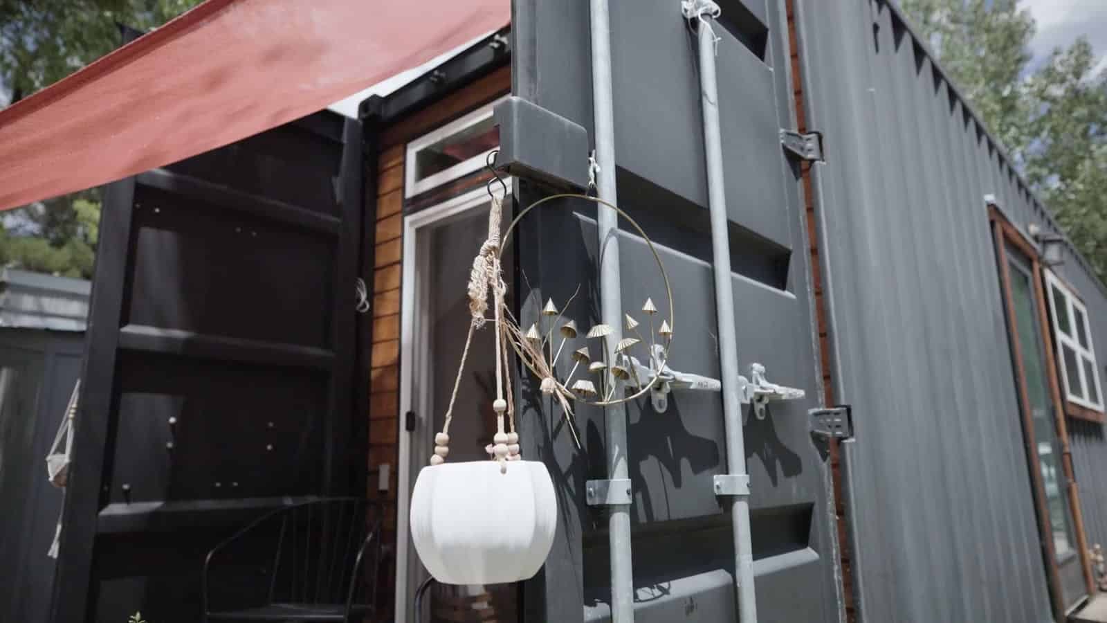 Close-up of the original shipping container cargo doors and locking bars on a container home, with a white hanging planter clipped to the latch