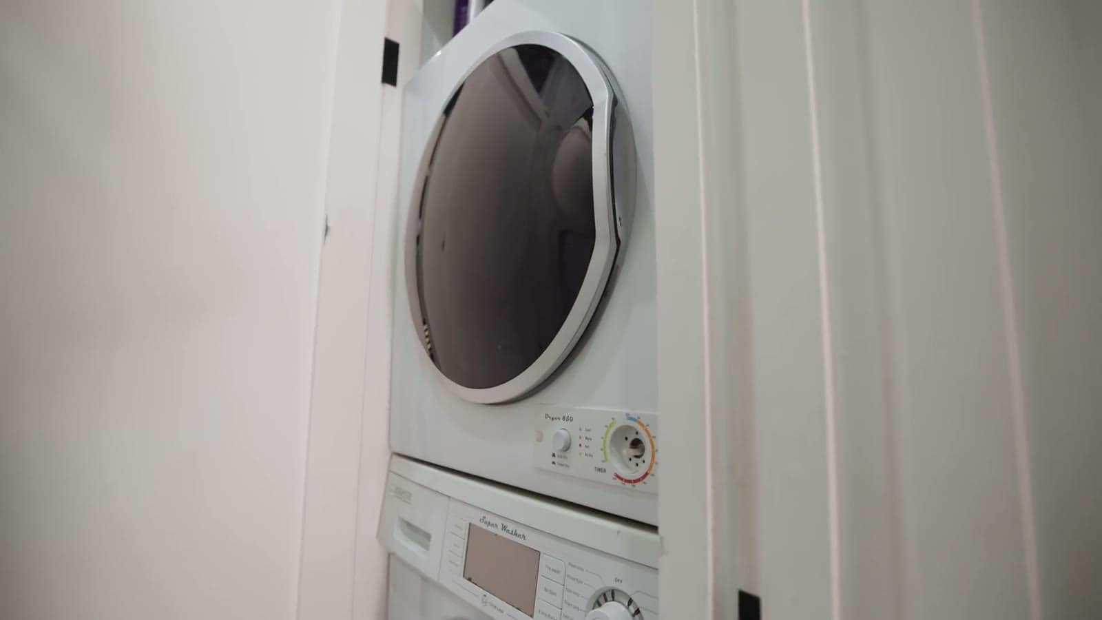 Compact stacked washer and dryer tucked into a white closet in a shipping container home