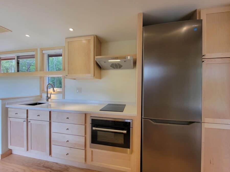 Interior of a tiny house kitchen with light wood cabinets and modern appliances.