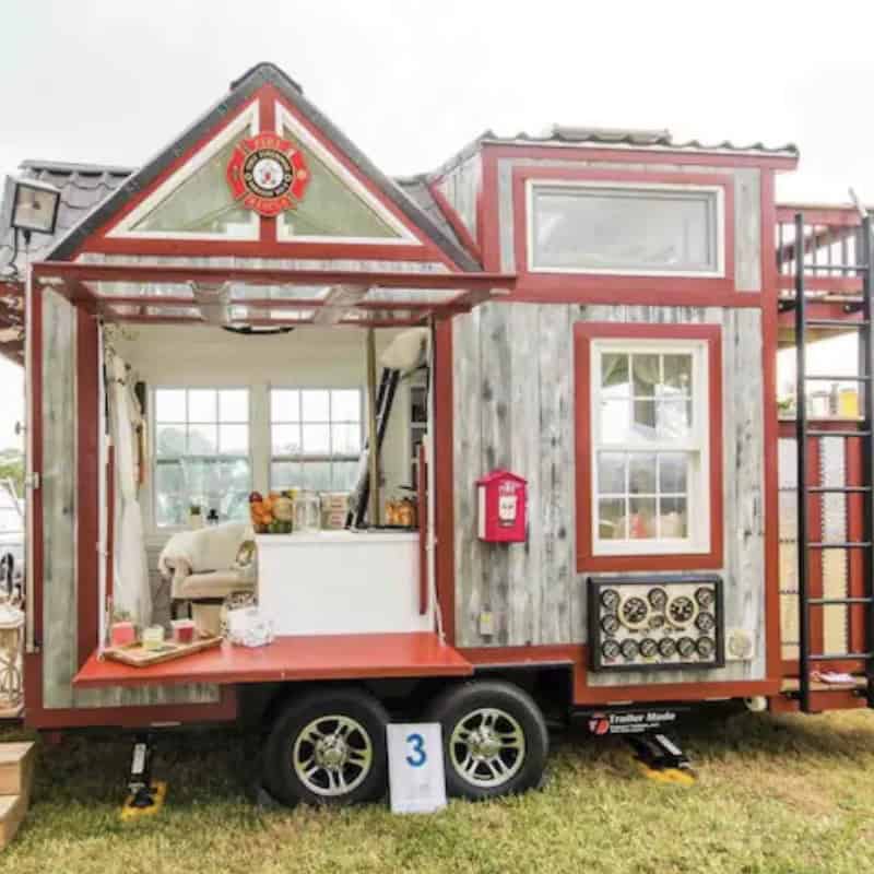 Firehouse-themed tiny house on wheels with reclaimed wood siding and a drop-down porch at a United Tiny House event