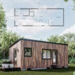 Modern tiny cabin on wheels with wooden exterior and large windows in a green outdoor setting.