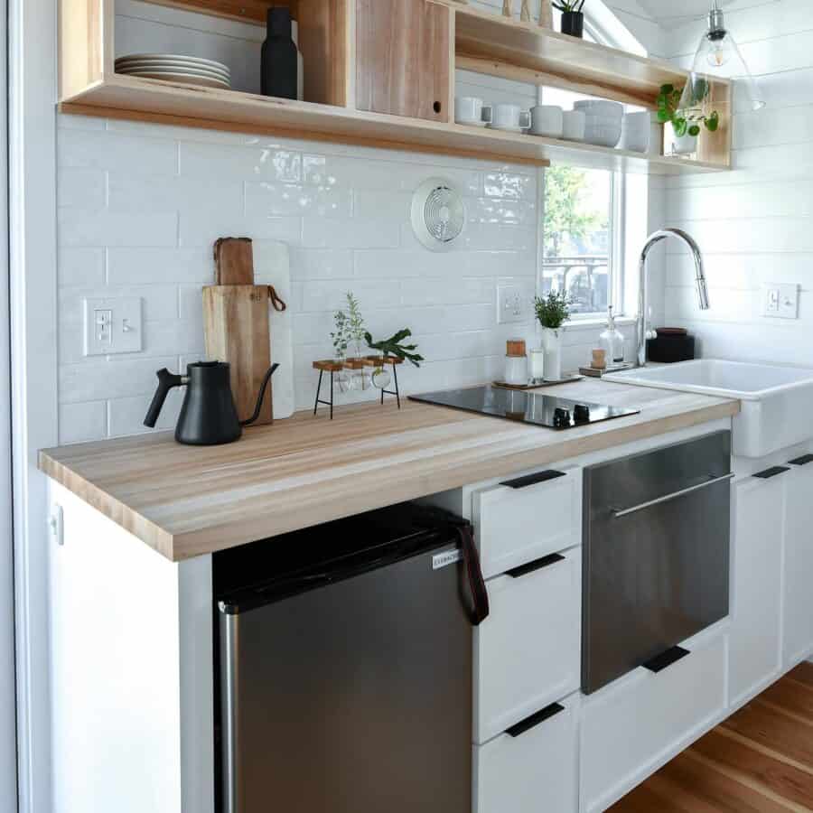 Modern tiny house kitchen with white cabinets, wooden countertop, and open shelving.