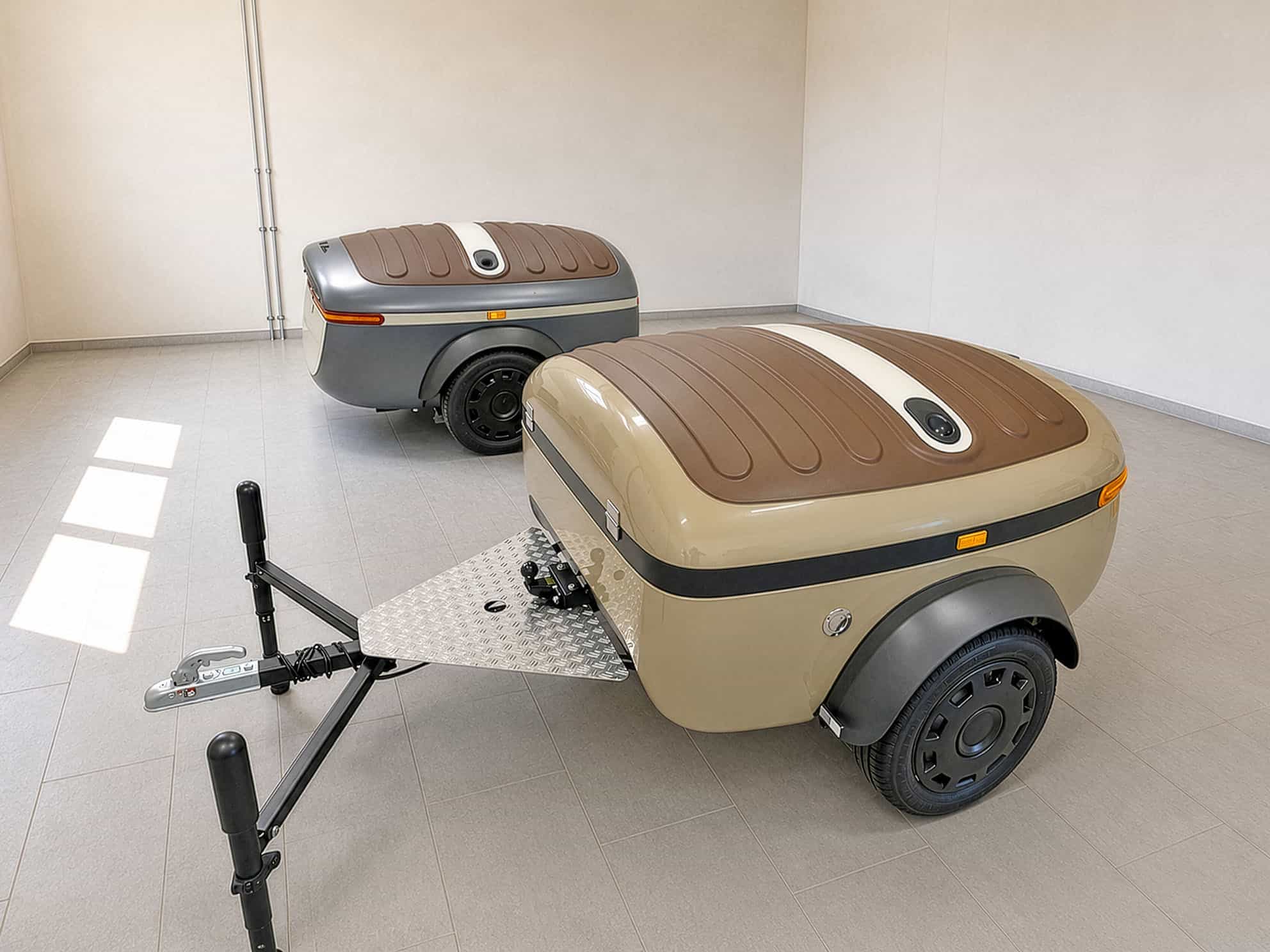Two closed Urbanoid Booba trailers in a showroom showing color options and the telescoping tow bar