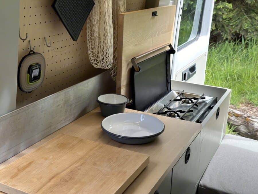 Compact van kitchen with built-in stove, minimalist design, and natural wood finishes.