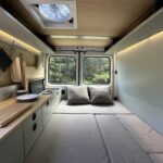 CNC-milled interior of a Sprinter van featuring minimalist design, solar power, and compact kitchen.