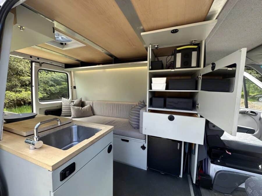 Sprinter van with CNC-milled wood interior, 200W solar, and minimalist kitchen setup.