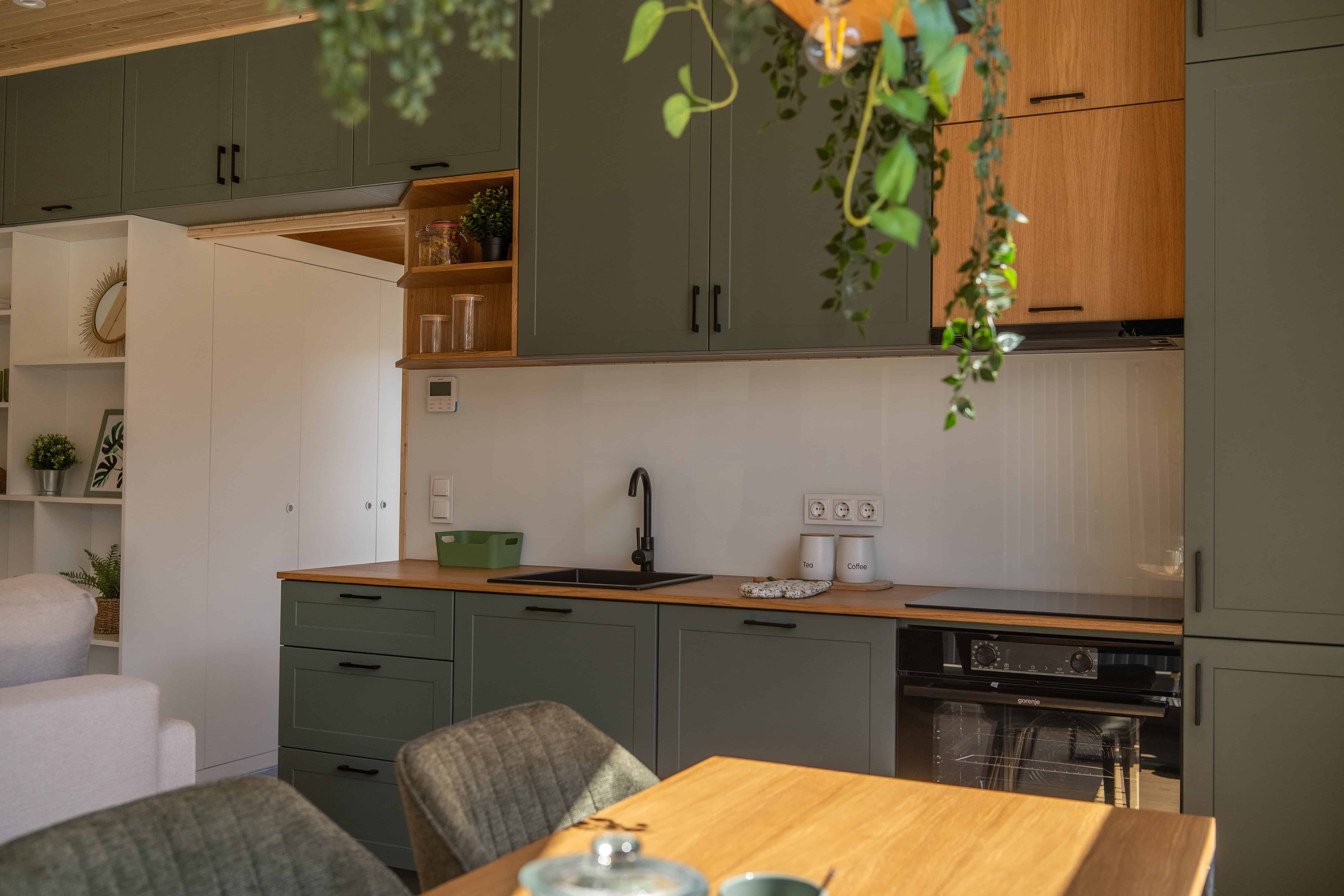 The dining area and green kitchen inside the Vagabond Haven Evergreen with a wood table and oak counters