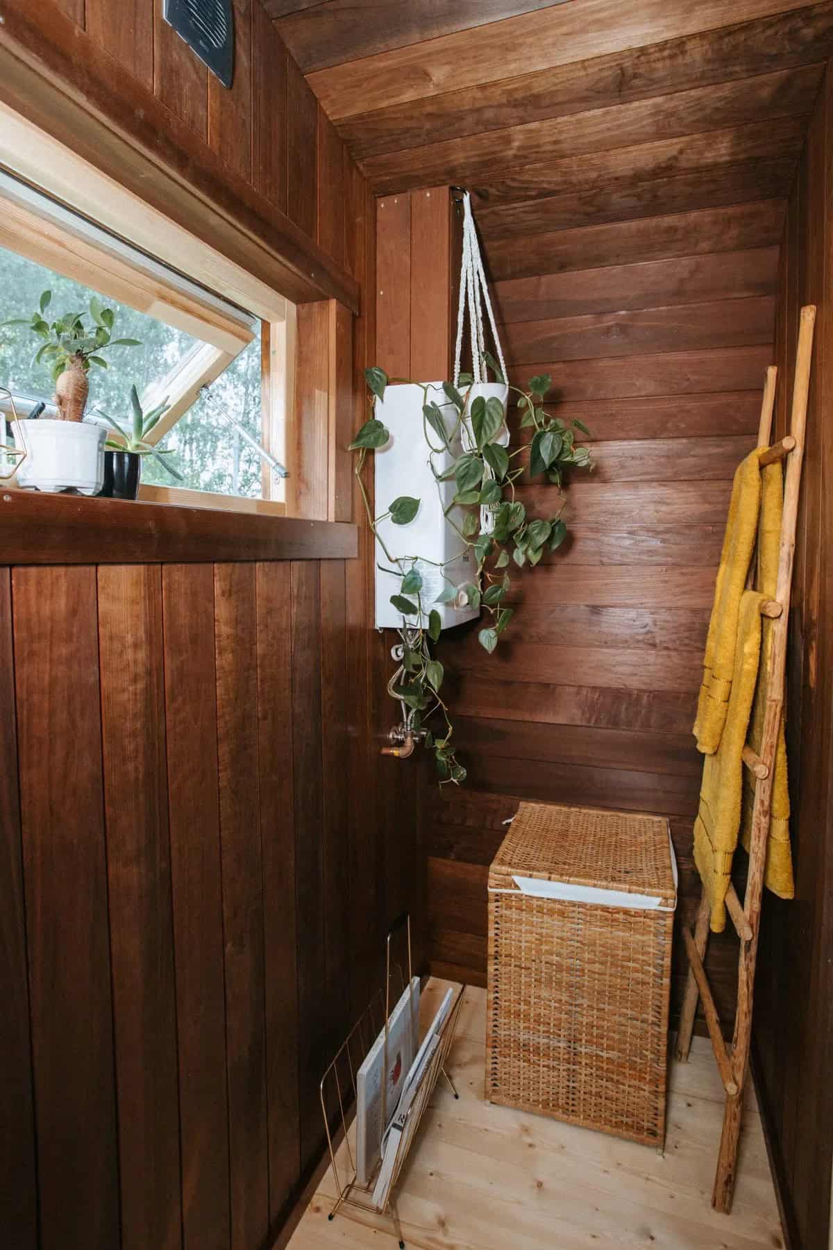 Corner of the Nature Pod bathroom with a small window, hanging plant, towel ladder, and wicker basket