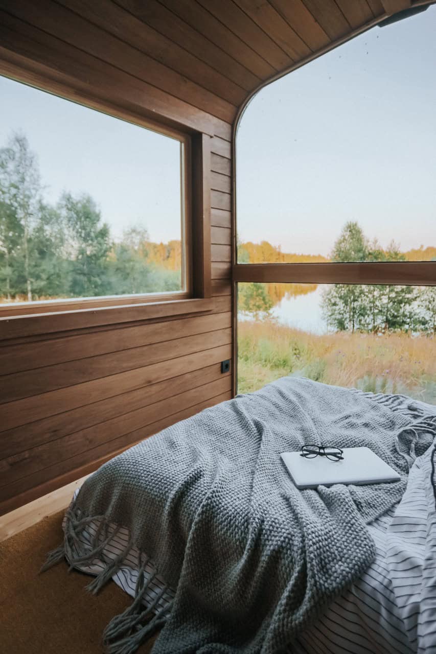 Corner windows beside the Nature Pod bed wrapping daylight around the wood-lined interior