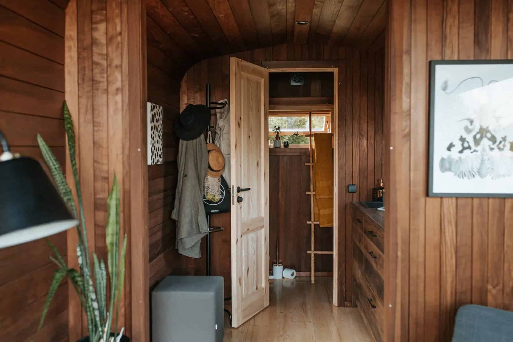 The Nature Pod entry with coat hooks, a wood door to the bathroom, a framed print, and a small hallway