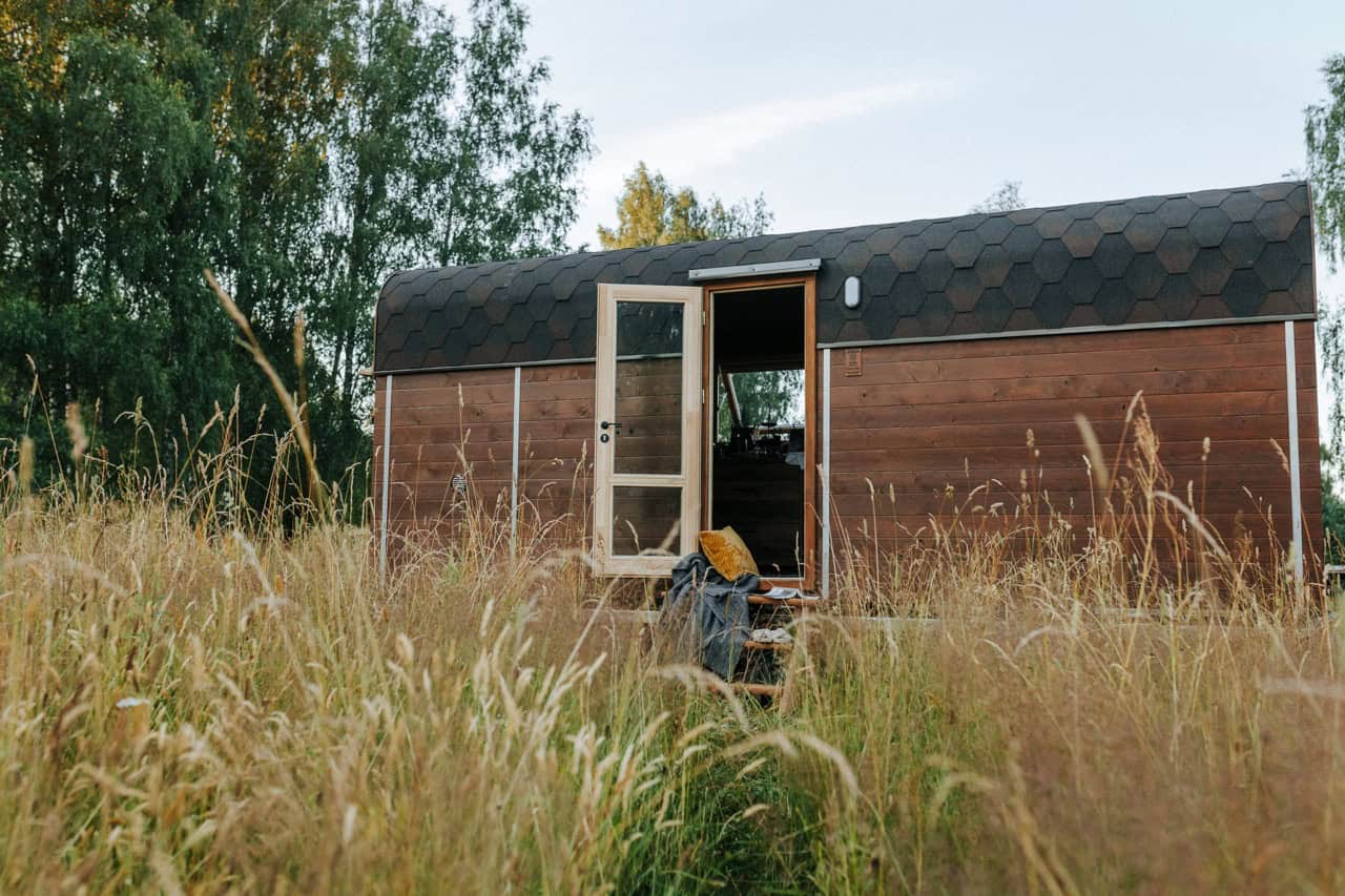 The Nature Pod by Vagabond Haven, a dark ThermoWood cabin with a curved shingle roof and full glass door, sitting in a meadow