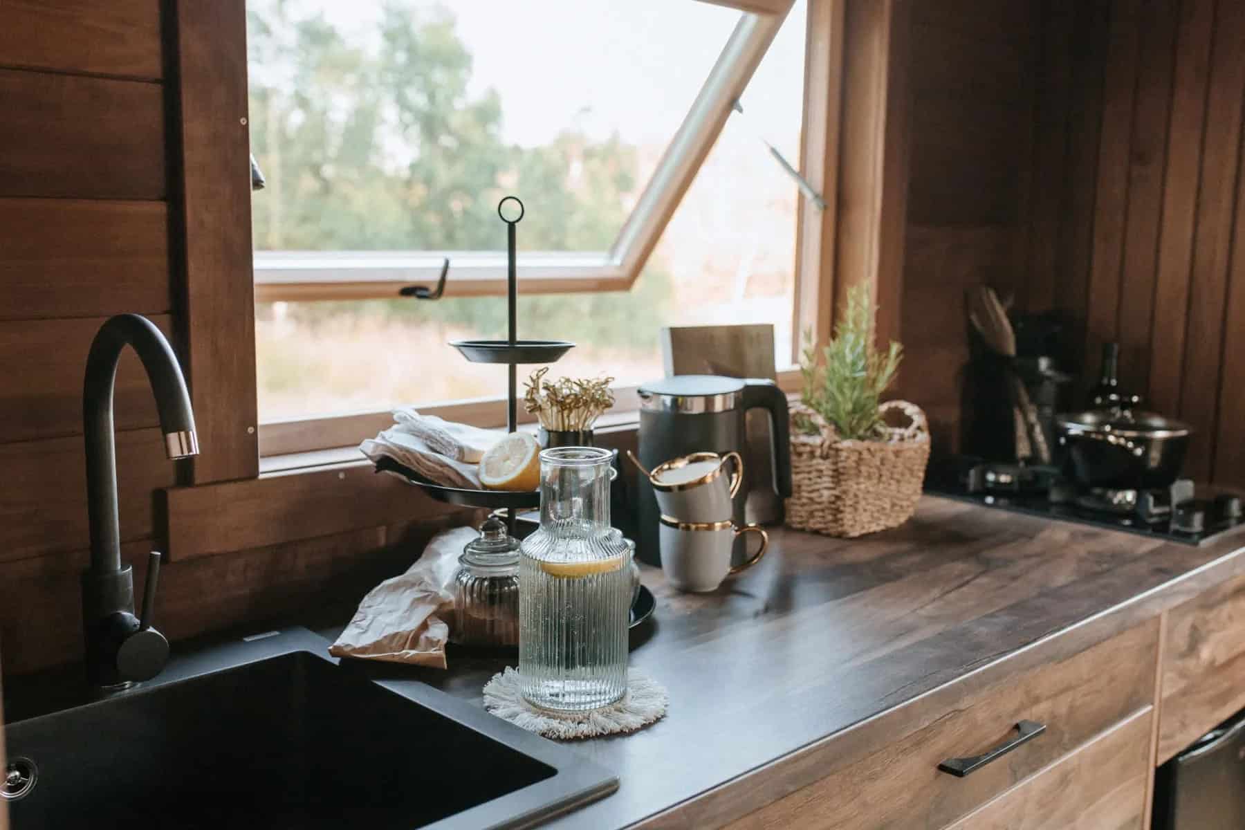 The Nature Pod's black kitchen sink and dark countertop under a tilt-open window with greenery outside