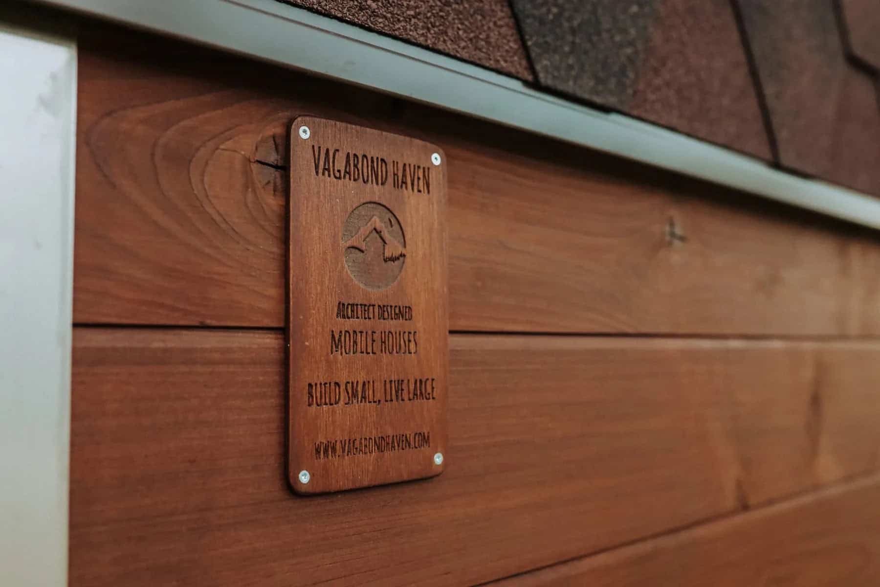 Close-up of the Nature Pod's ThermoWood siding with a carved Vagabond Haven maker's plaque under the shingle roof edge