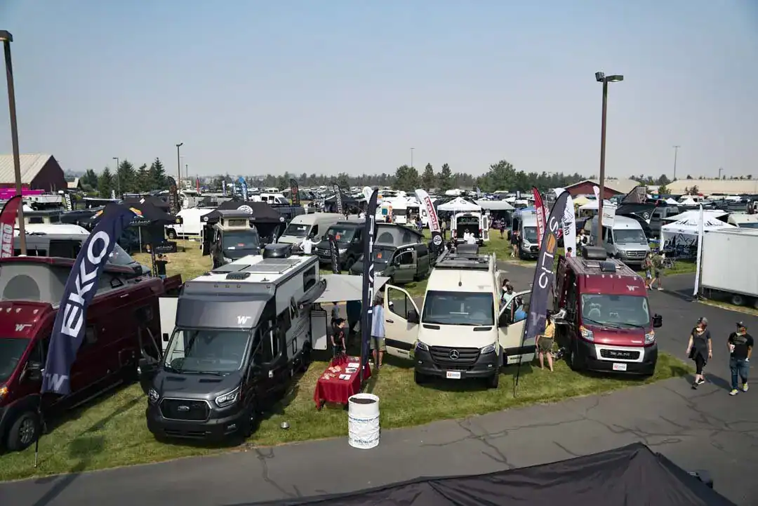 Vans and camper rigs parked in a grass field at an outdoor van life gathering