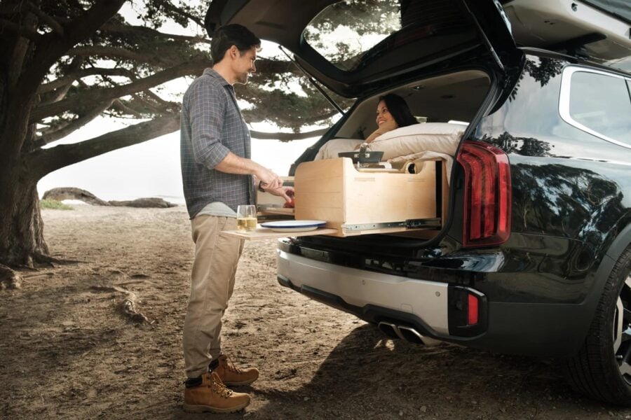 Couple enjoying outdoor meal from tiny house with open trunk.