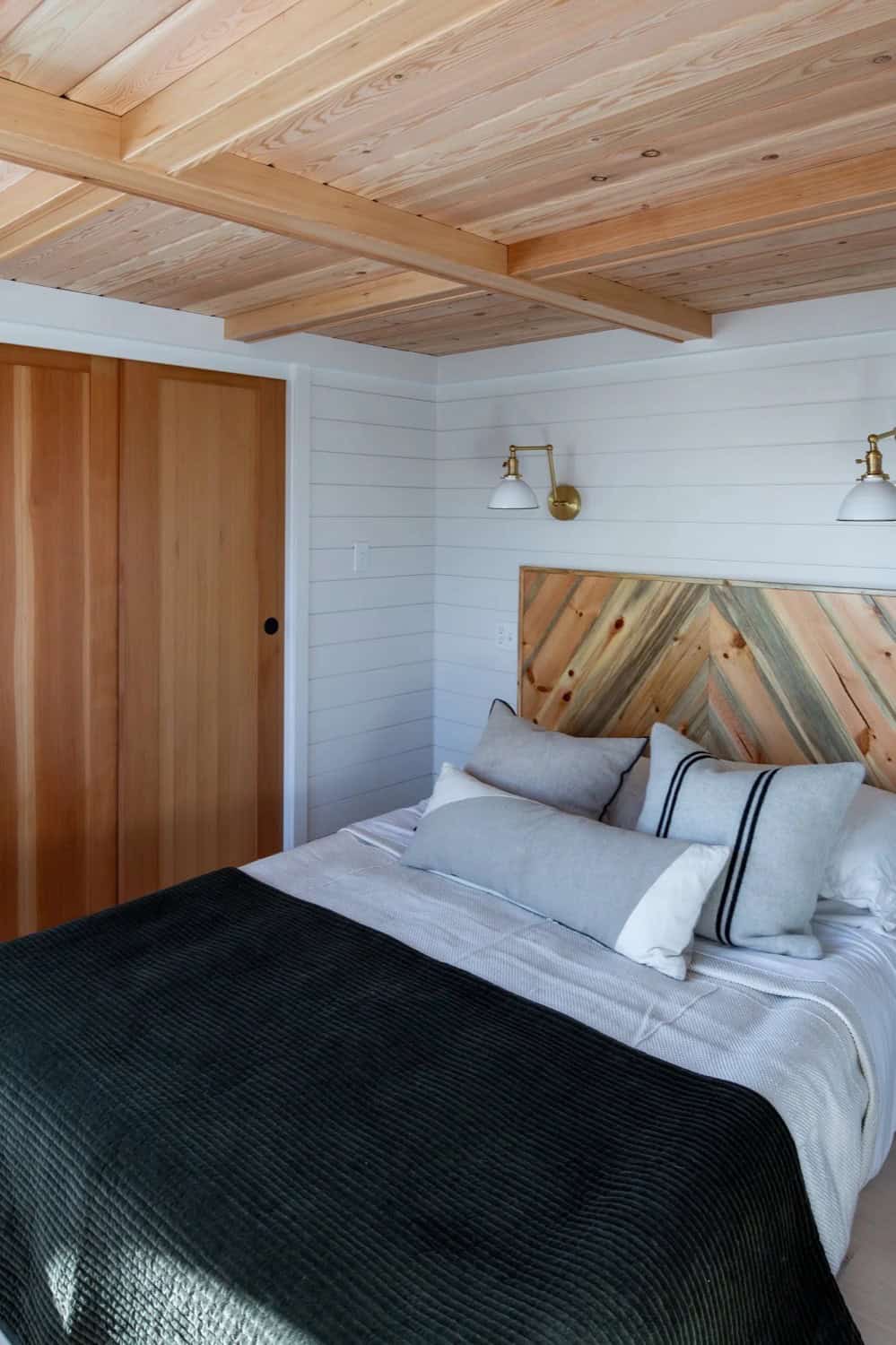 Main-floor bedroom in the Villa Max with chevron wood headboard, plank ceiling and brass sconces