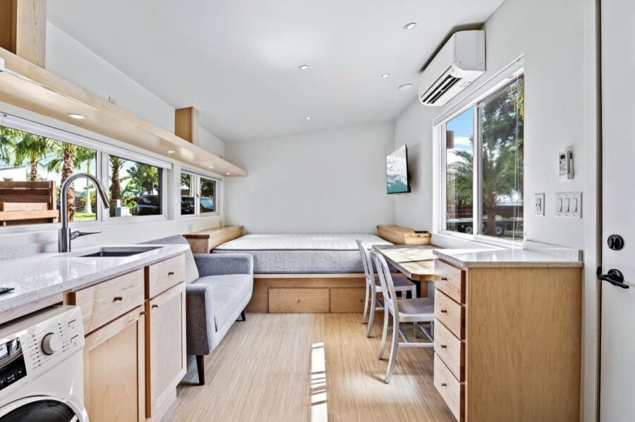 Bright tiny house interior featuring a compact kitchen, cozy sleeping nook, and large windows with n.