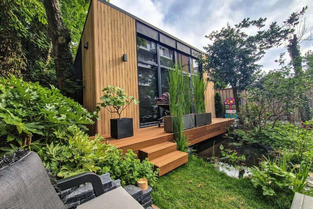 Modern tiny house with large glass wall and wooden exterior in lush garden setting.
