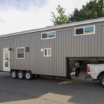 Modern tiny house on wheels connected to a pickup truck, ideal for mobile living and small space fre.
