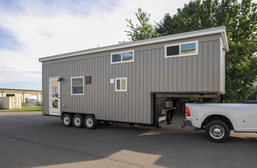Modern tiny house on wheels connected to a pickup truck, ideal for mobile living and small space fre.