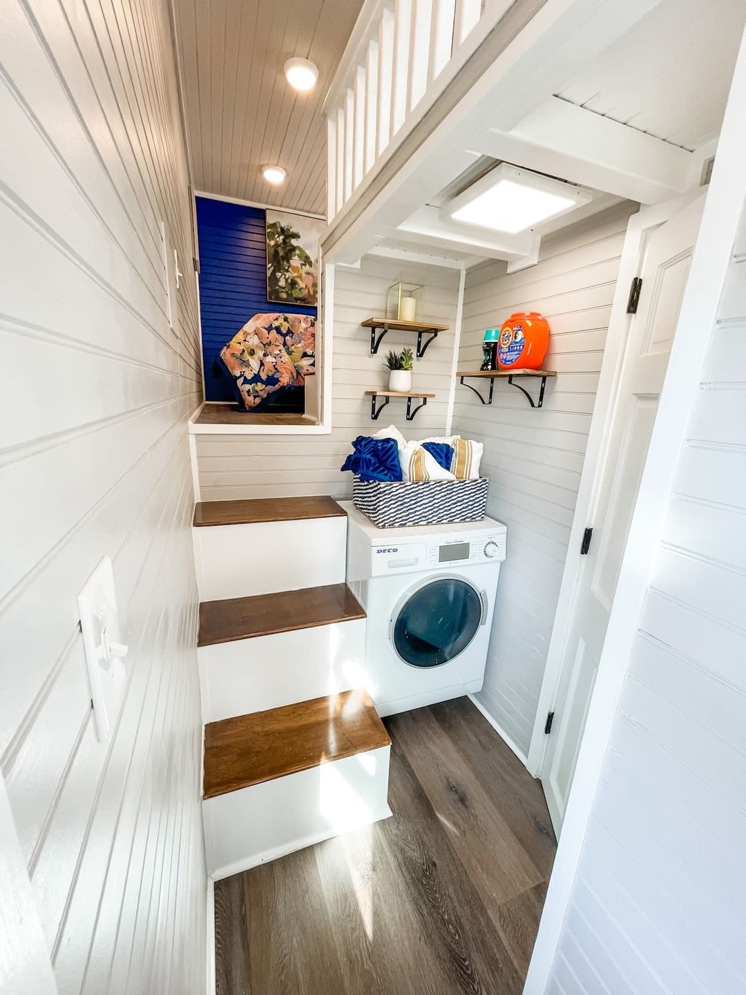 Compact laundry space with stairs and shelves in tiny house interior.