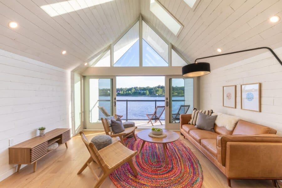Bright waterfront cabin living room with large windows and modern decor.