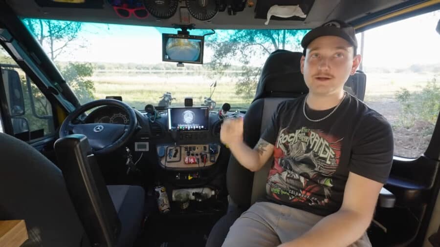 Interior view of a tiny van home built on a T1N Sprinter chassis with a young man inside.