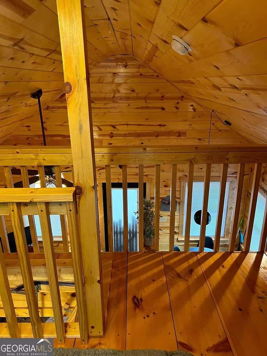 Loft interior with warm wood paneling and railing in Whispering Hills Cabin among trees.