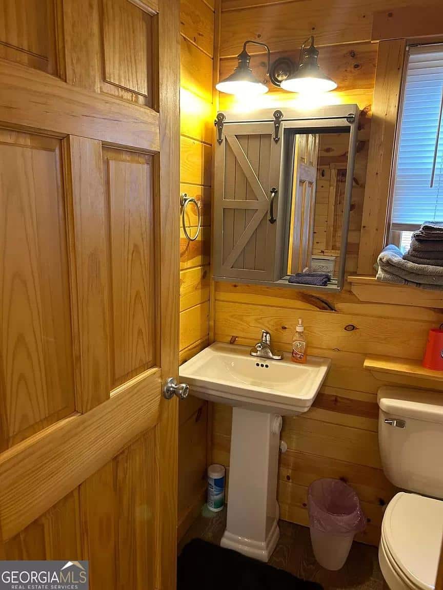 Small rustic bathroom with wooden walls, a pedestal sink, and a mirror with barn door style cabinet.