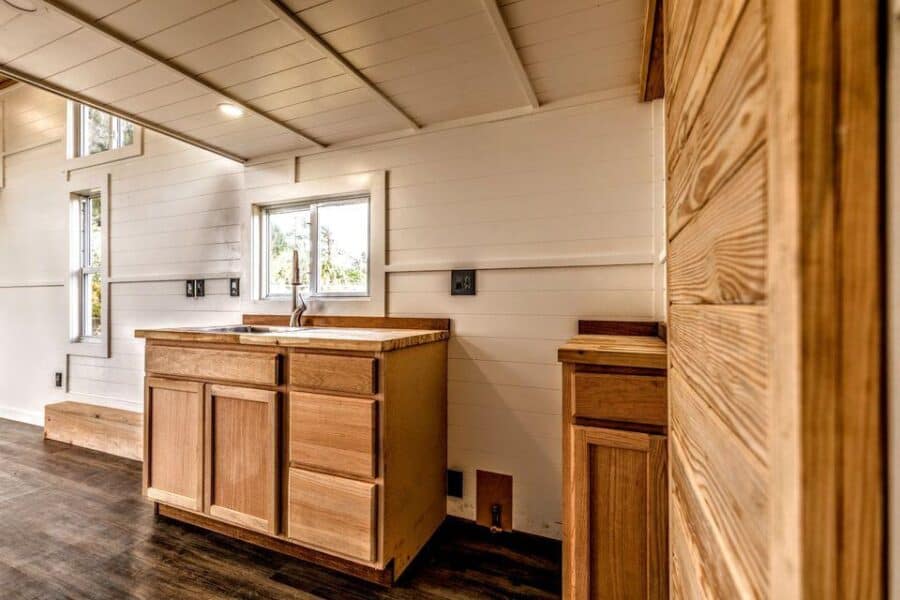 Interior view of a compact tiny house kitchen with wooden cabinets and natural light.