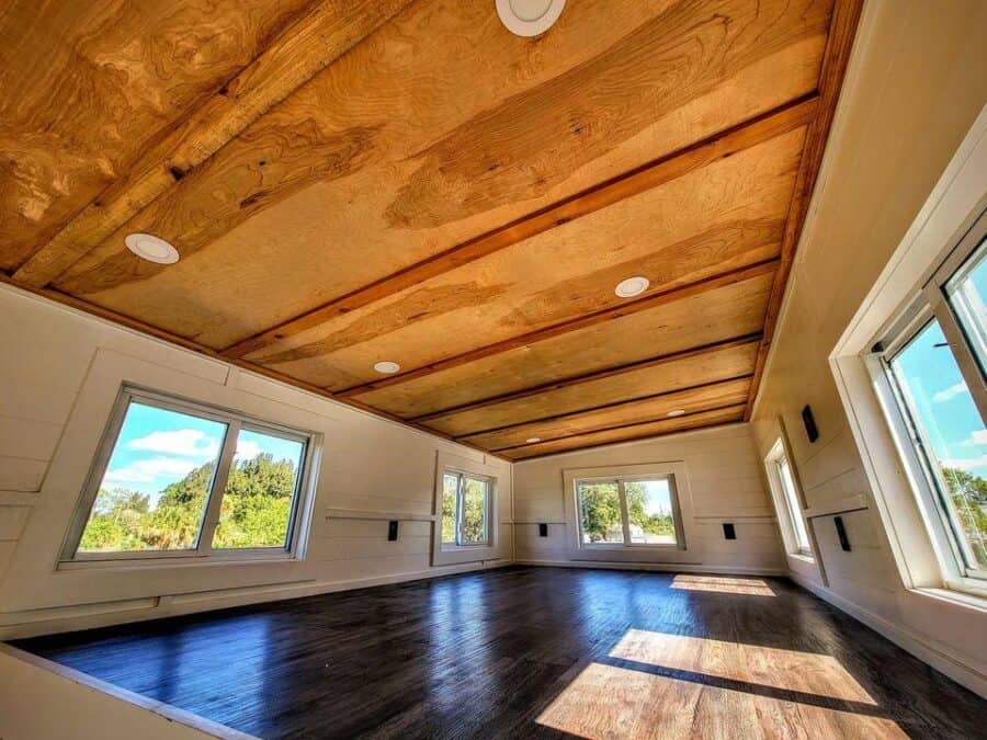 Spacious tiny house interior with wooden ceiling and large windows for natural light.