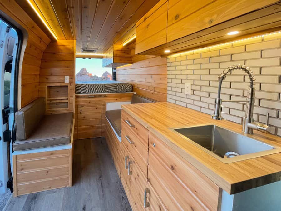 Compact camper van kitchen with wooden cabinets and modern sink setup.