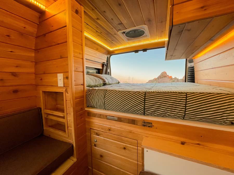 Compact tiny house bedroom with wood interior and scenic mountain backdrop.