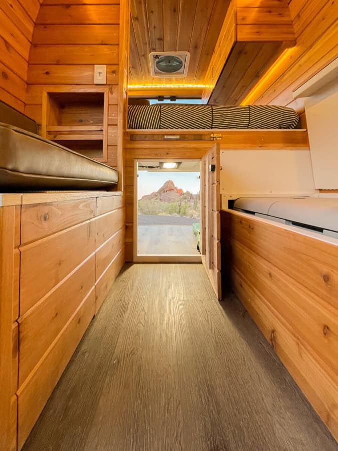 Interior view of a cozy wooden tiny house with built-in storage and a sleeping loft.