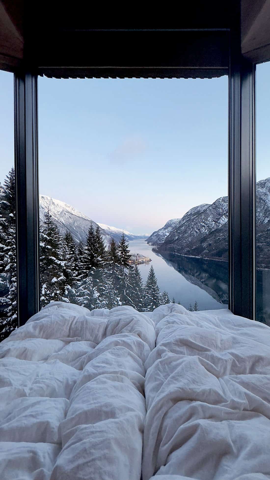View from the bed inside a Woodnest Treehouse looking out at the fjord and mountains in winter