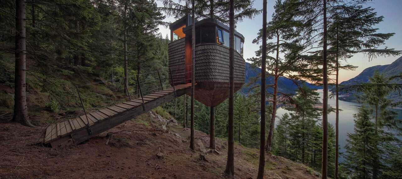 Woodnest Treehouse with timber bridge walkway and fjord views at sunset in Odda Norway