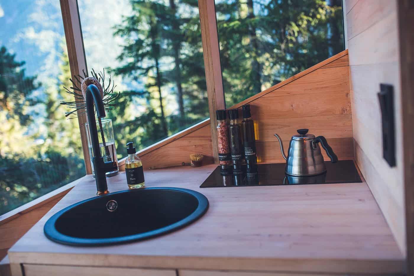 Kitchenette detail in the Woodnest Original cabin with black sink, cooktop, and forest view through glass