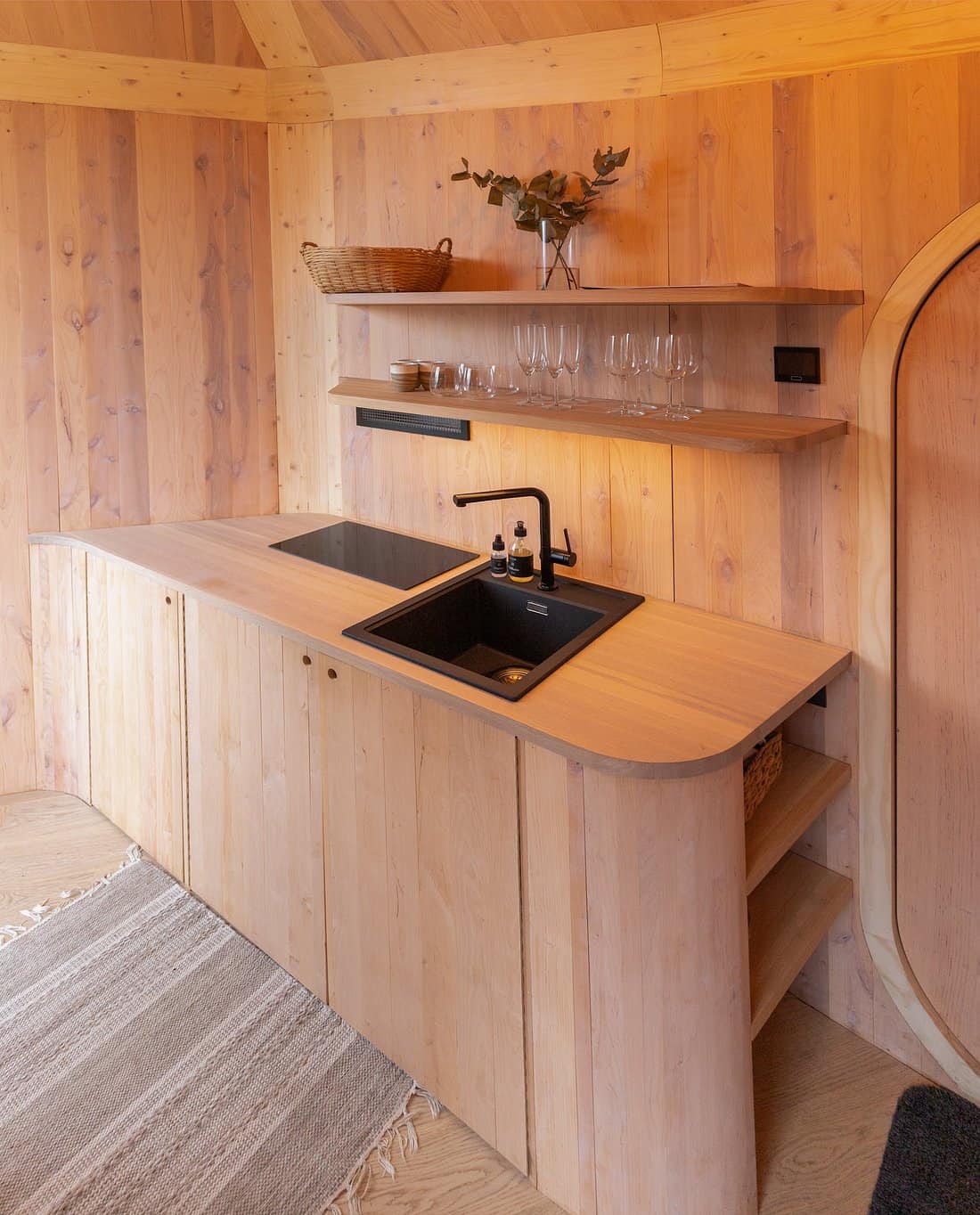 Mountaintop cabin kitchenette with all-wood interior, floating shelves, and black sink at Woodnest