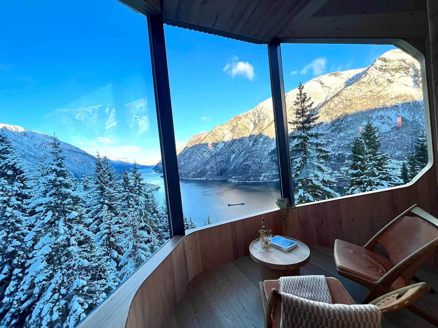 Panoramic winter fjord and mountain view from inside a Woodnest Mountaintop treehouse with chairs and side table