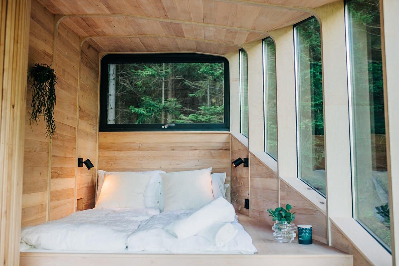 Queen bed inside the Woodnest Original cabin with curved wood walls and glass panels overlooking forest