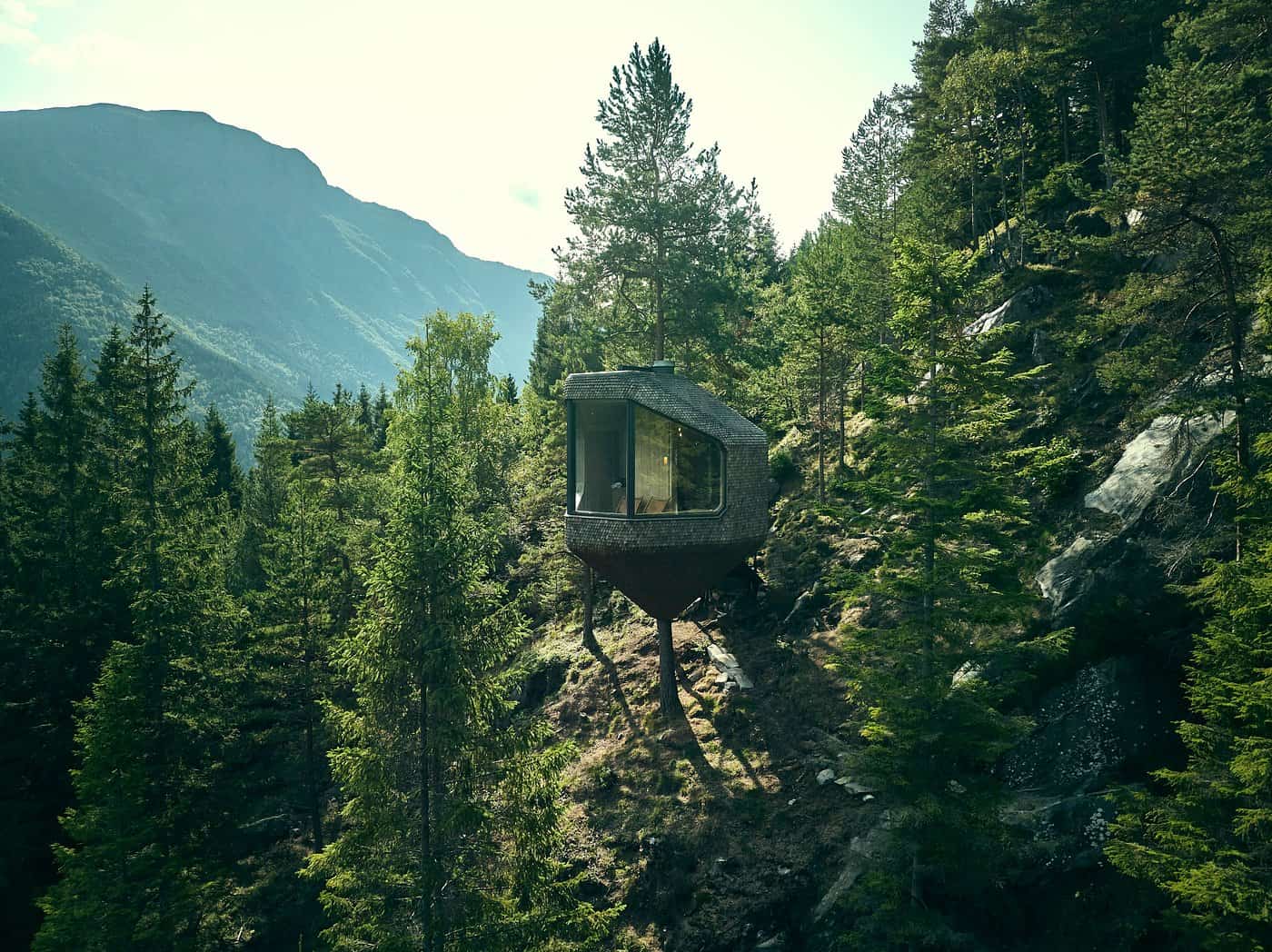 Woodnest Treehouse on a hillside in summer with mountains and green forest in Odda Norway