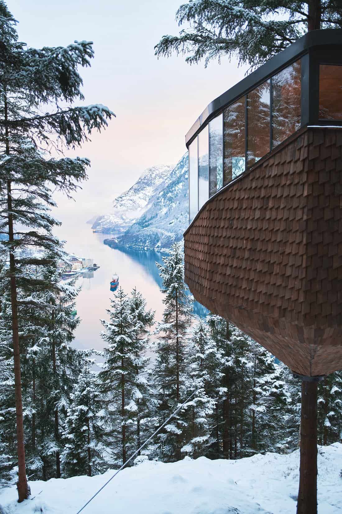 Woodnest Treehouse exterior in winter with shingle cladding, fjord, and snow-covered trees