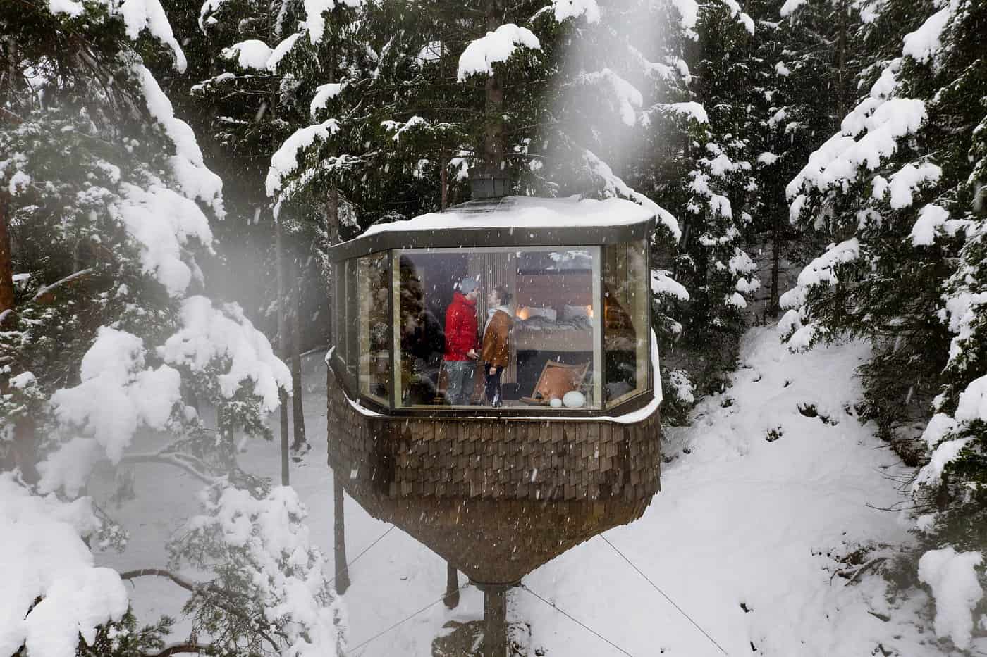 Woodnest Treehouse Original cabin in winter with snow on pine trees and guests visible inside
