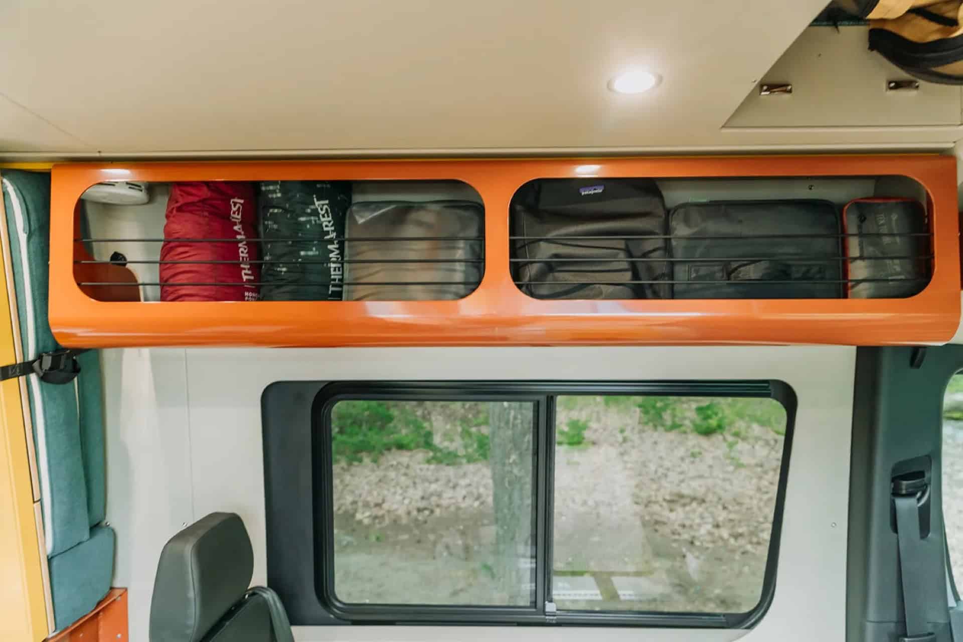 Orange overhead storage shelf in GB01 with bungee netting holding stuff sacks above a window