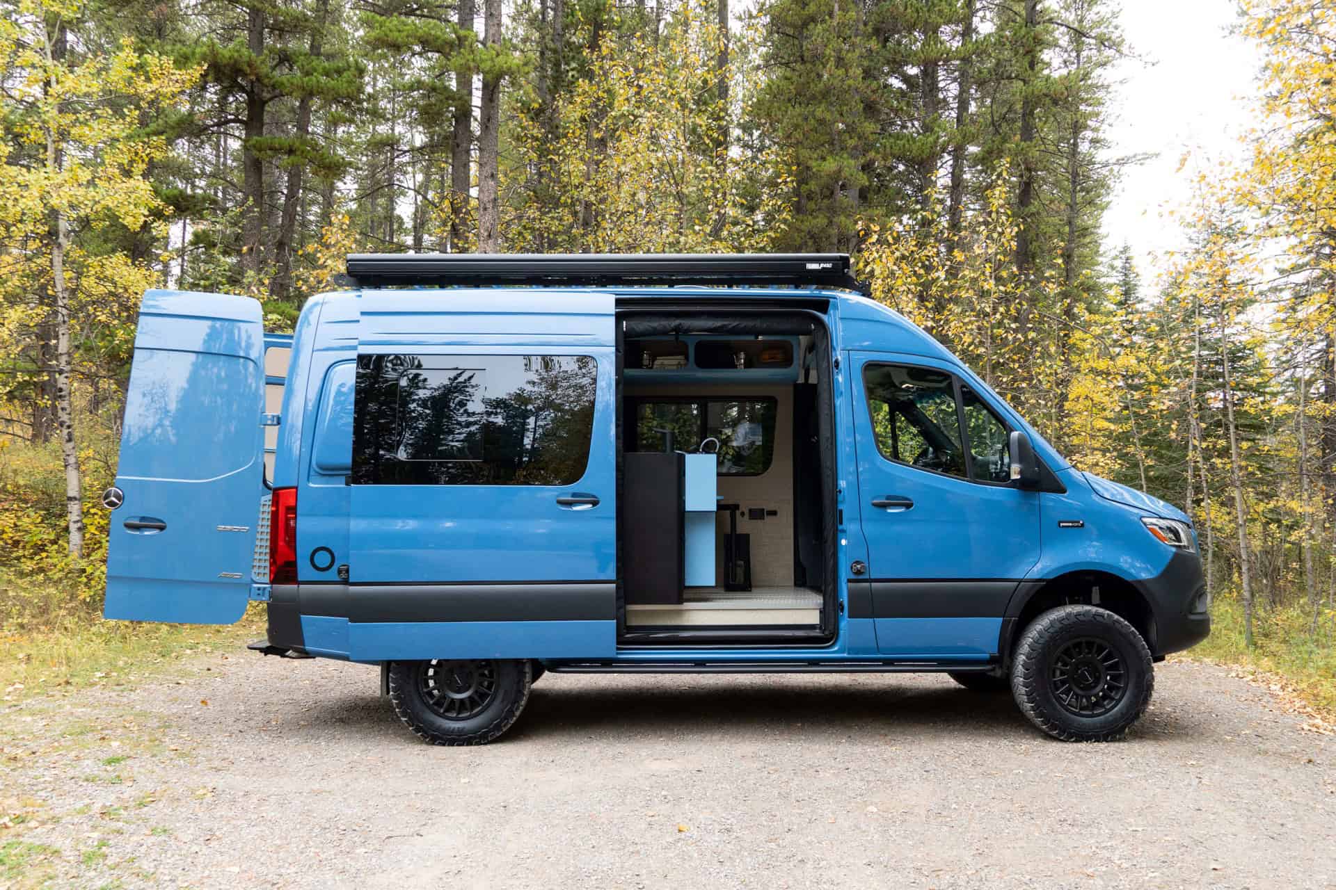 Blue Yama Vans Gear Bus Peyto AWD Sprinter camper van parked in a forest with its doors open