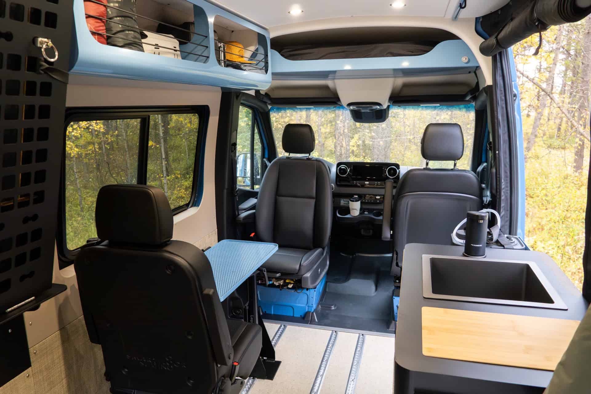 Interior of the Peyto camper van with swiveling captain's seats, a small table, and a galley with a sink